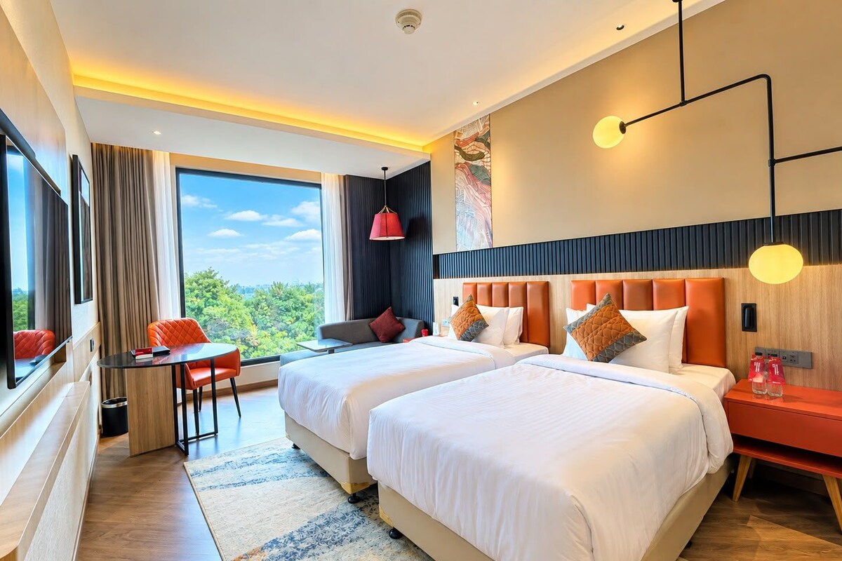 A hotel room with two beds, a desk, and a view of the outdoors.