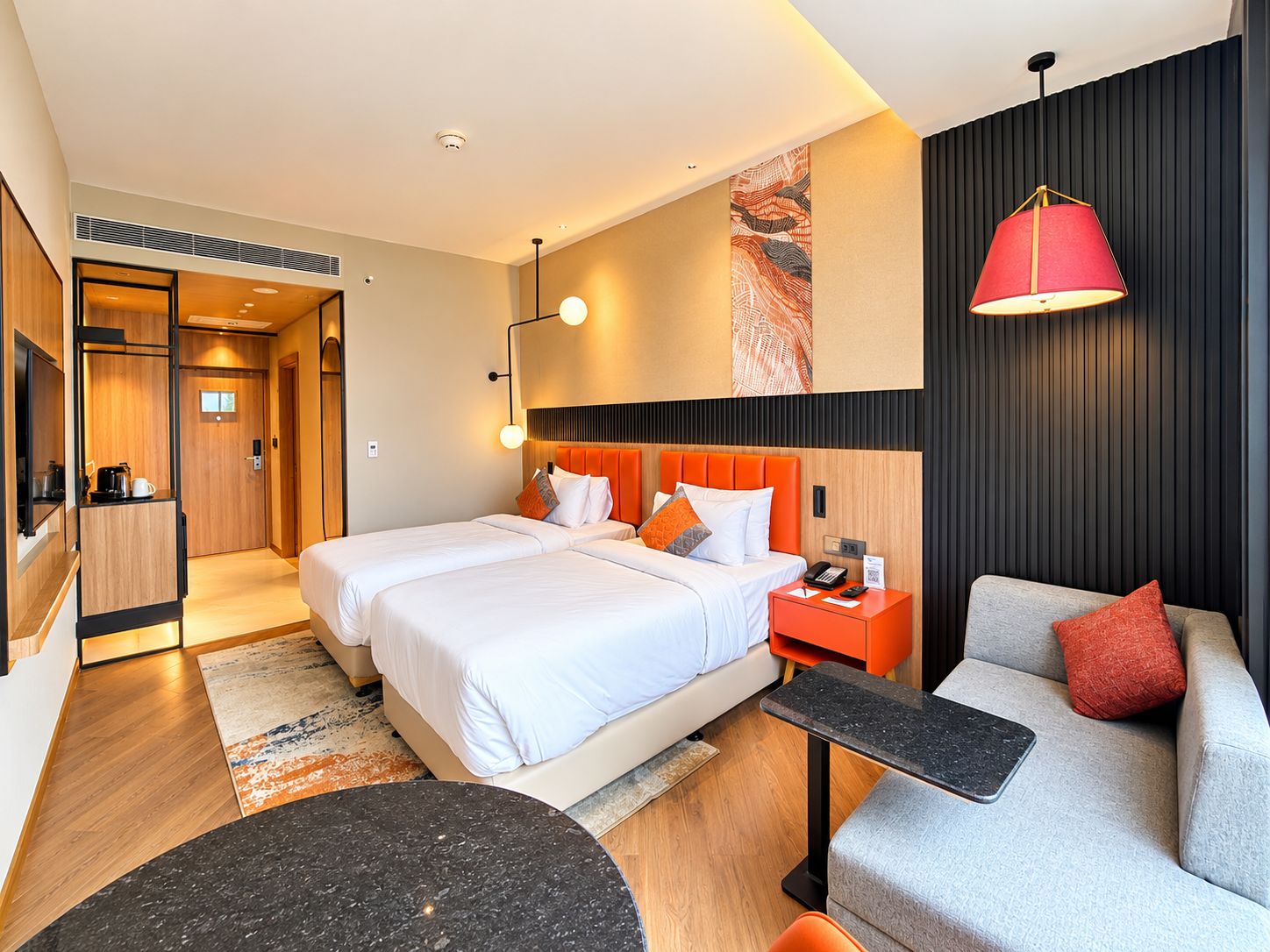 A hotel room with a double bed, a desk, a chair, a small table, and a sofa.