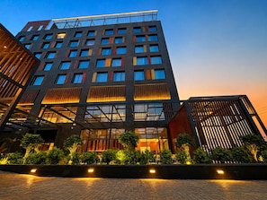 Um hotel com vários andares e design arquitetônico moderno, com uma fachada de vidro marcante e um terraço no telhado.