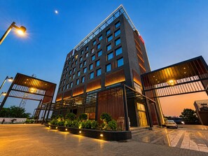 Un hotel modern amb una entrada destacada, diverses plantes i una façana ben il·luminada.