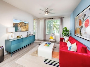 A modern living room with a red sofa, a white coffee table, a teal cabinet, and a ceiling fan. - Spacious 2BR Stay w Pool at Embark Apartments (Fremont)
