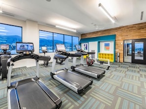 A gym with treadmills, exercise bikes, and a large window with a city view. - Spacious 2BR Stay w Pool at Embark Apartments (Fremont)
