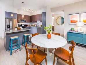 A modern kitchen with stainless steel appliances, a marble island, and wooden chairs. - Spacious 2BR Stay w Pool at Embark Apartments (Fremont)