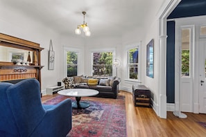 A living room with a sofa, a coffee table, a rug, a wooden cabinet, and a large window. - North End Retreat Near Hyde Park (Boise)