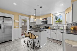 A modern kitchen with white cabinetry, a central island, bar stools, and a window with a view. - North End Retreat Near Hyde Park (Boise)