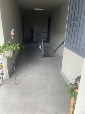 Um corredor estreito com corrimão de metal, escada e plantas em vasos.