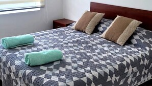 A neatly made bed with a geometric patterned bedspread, two pillows, and two rolled towels. - Cabin in Coyhaique: Explore the Carretera Austral (Coyhaique)