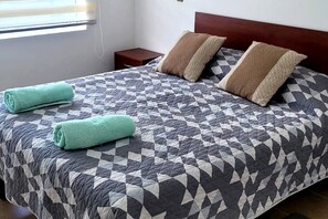 Ein ordentlich bezogenes Bett mit einem geometrisch gemusterten Überwurf, zwei Kissen und zwei aufgerollten Handtüchern.