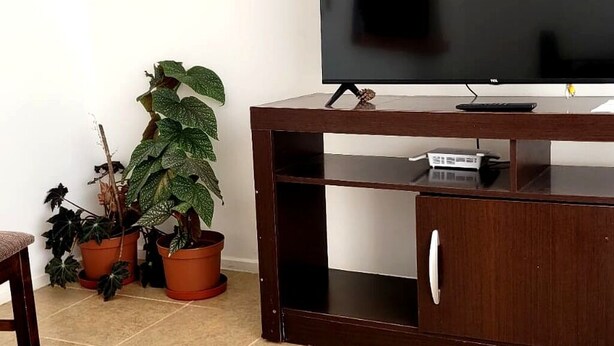 A wooden TV stand with a flat-screen TV, a remote control, and a small electronic device on top. - Cabin in Coyhaique: Explore the Carretera Austral (Coyhaique)