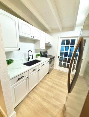 Eine Küche mit weißen Schränken, einem Edelstahlkühlschrank und einem Fenster mit Jalousien.