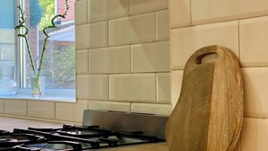 Une cuisine équipée d’une cuisinière à gaz, d’une planche à découper en bois et d’une fenêtre donnant sur un paysage verdoyant.