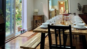 Un espace repas avec une longue table dressée pour le repas, un banc en bois et une vue sur la verdure à l’extérieur.