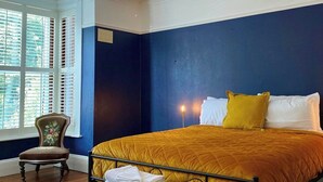 Une chambre à coucher comprenant un lit, une chaise, un banc, un plafond décoratif et une fenêtre avec des volets.