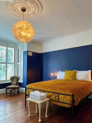 Ein Schlafzimmer mit Bett, Stuhl, Sitzbank, dekorativer Decke und Fenster mit Rollläden.