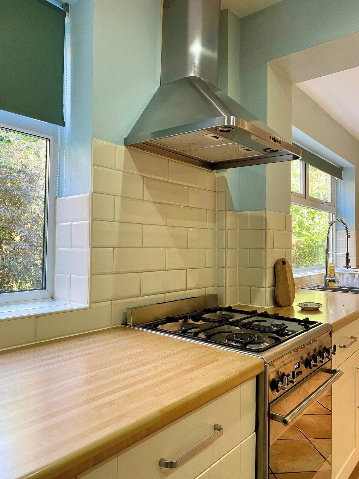 A kitchen with a gas stove, a stainless steel range hood, and a window with a view of trees.