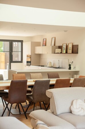 Een moderne keuken met witte kasten, een eethoek met lederen stoelen en een bank met een witte kussens.