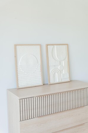 Zwei gerahmte Wandbilder auf einer hellen Holzkommode vor einer schlichten Wand.