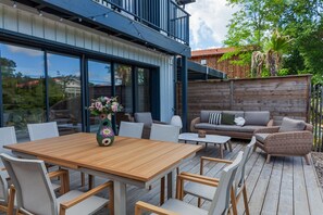 Een terras buiten met een houten tafel en stoelen, een bank en een decoratieve vaas.