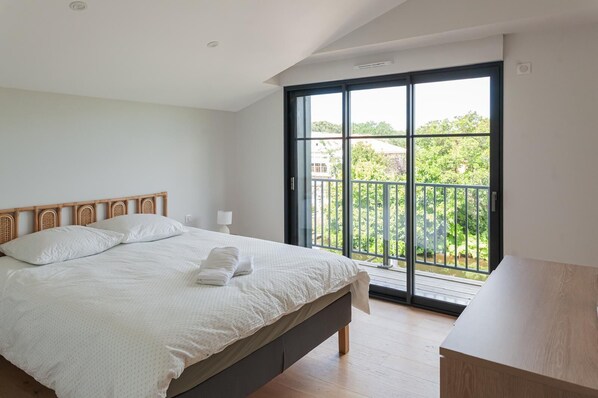 Een slaapkamer met een bed, nachtkastje, raam met uitzicht op groen en een balkon.