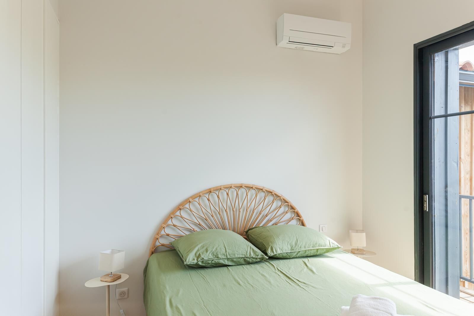 Un dormitorio con una cama, una mesita de noche, aire acondicionado instalado en la pared y una ventana.