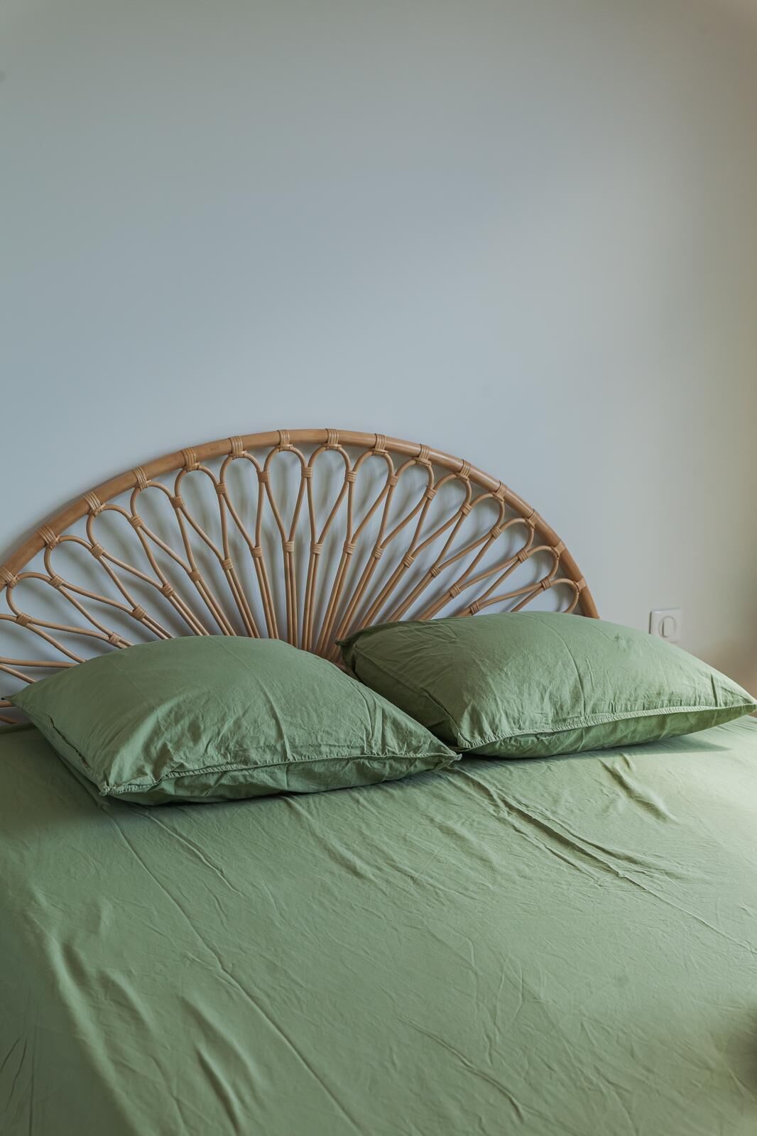 Un lit avec une tête de lit en osier, deux oreillers et une couvre-lit verte.
