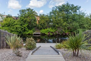 A wooden dock leading to a small wooden structure surrounded by lush greenery and a body of water. - Villa Cazora – Terrace & Canal View in Cazaux (La Teste-de-Buch)