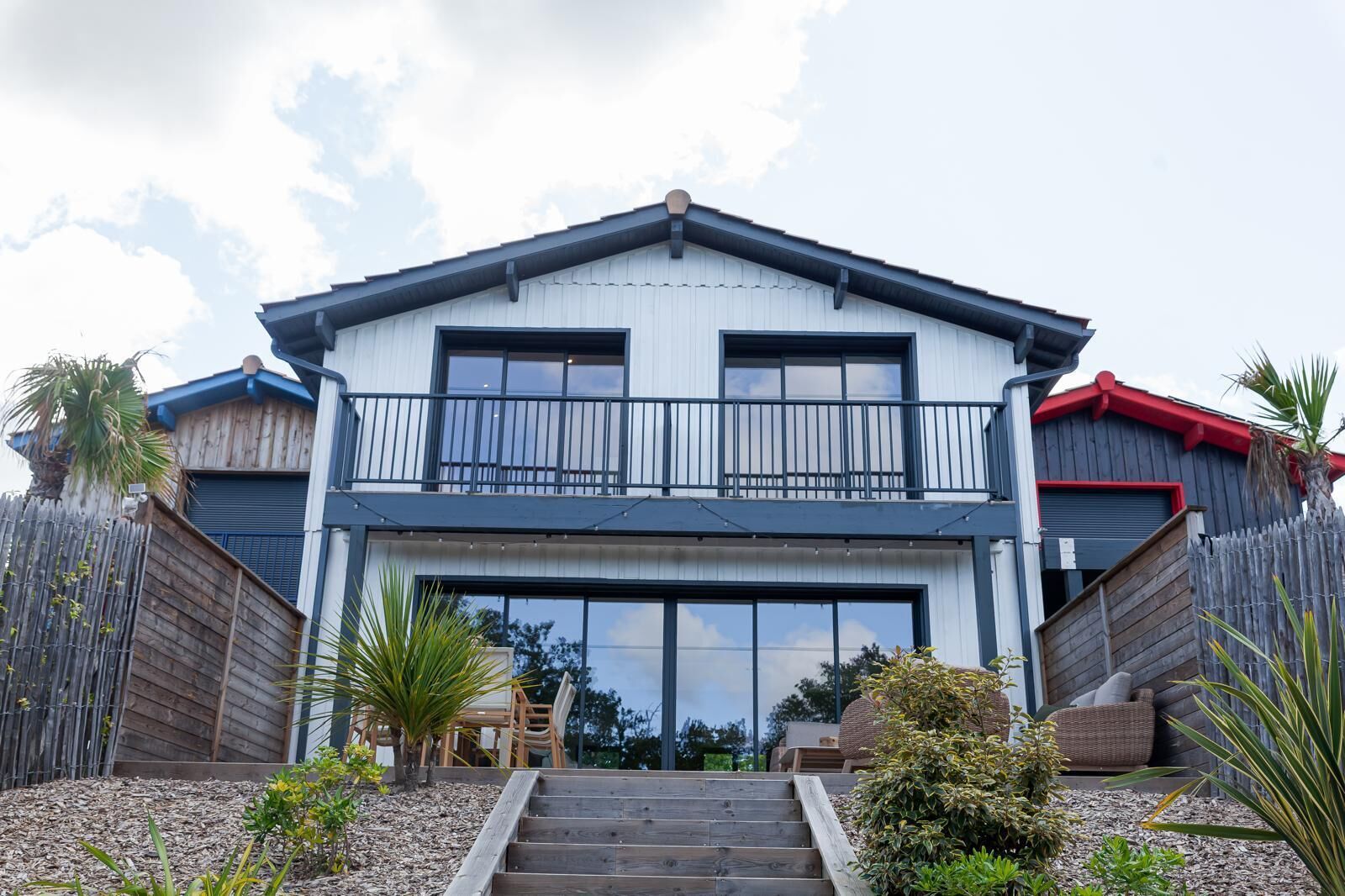 Ein zweistöckiges Haus mit Balkon, Garage und einem Vorgarten mit Pflanzen.