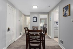 Un pasillo con una mesa de comedor y sillas, puertas blancas y un reloj en la pared.