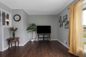 Ein Wohnzimmer mit Flachbildfernseher, einer Uhr, einem Blumentopf und Kunstwerken an den Wänden.