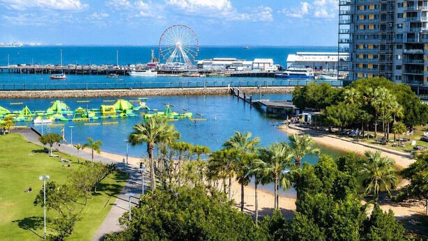 A coastal view with a Ferris wheel, a marina, and a hotel with multiple floors and balconies. - Tropical Breeze Poolside Stay near the Waterfront (Parap)