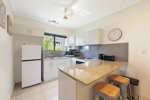 A modern kitchen with white cabinets, a granite countertop, a built-in oven, and a clock on the wall. - Tropical Breeze Poolside Stay near the Waterfront (Parap)