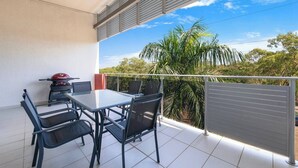 A balcony with a table and chairs, a grill, and a view of palm trees and greenery. - Tropical Breeze Poolside Stay near the Waterfront (Parap)