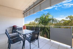 A balcony with a table and chairs, a grill, and a view of palm trees and greenery. - Tropical Breeze Poolside Stay near the Waterfront (Parap)
