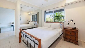 A bedroom with a bed, bedside table, mirror, window with view, ceiling fan, and air conditioning unit. - Tropical Breeze Poolside Stay near the Waterfront (Parap)