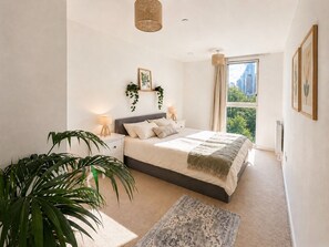 Ein Schlafzimmer mit einem großen Bett, Nachttischlampen, Blick auf die Stadt und einer Zimmerpflanze.