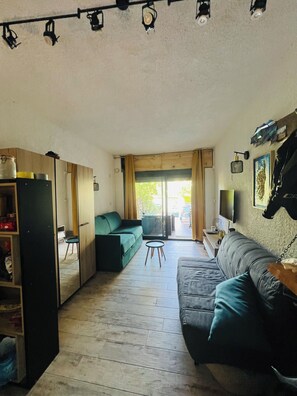 Ein gemütlicher, kompakter Wohnbereich mit Sofa, kleinem Tisch, Schrank und Fernseher.