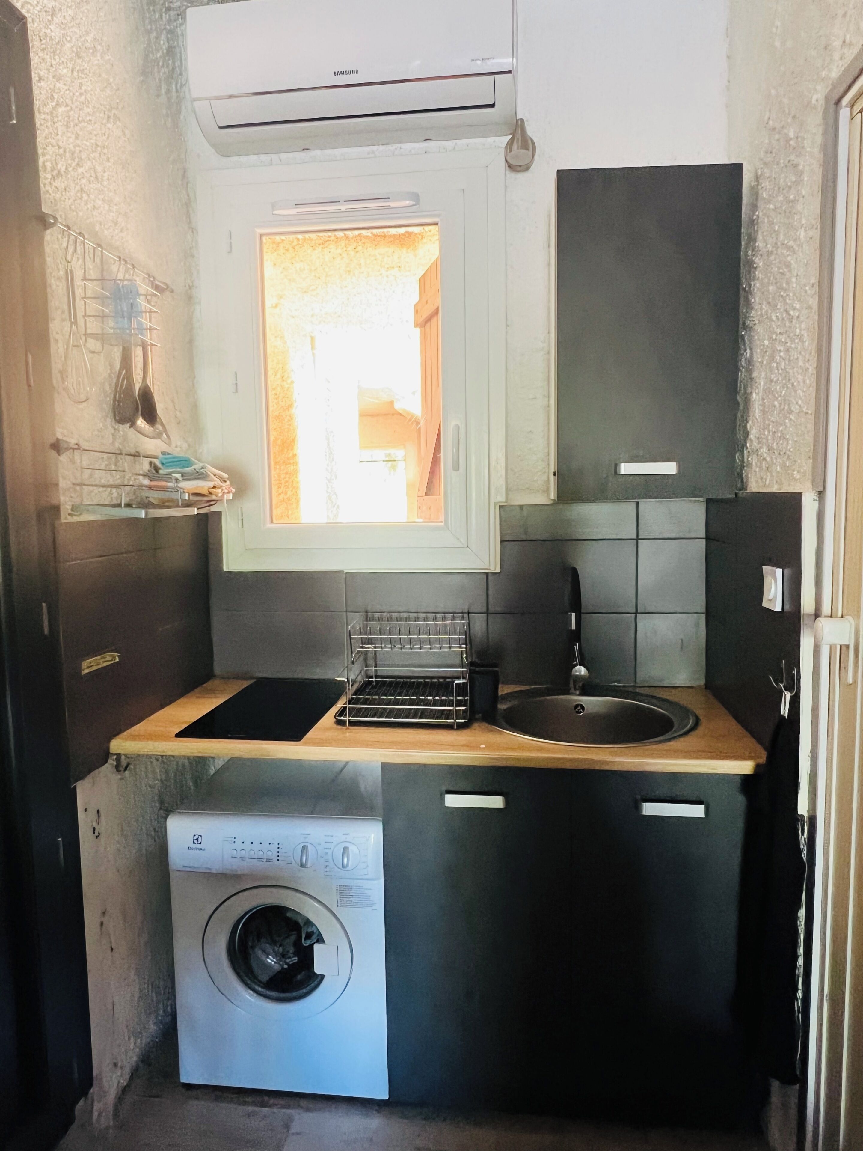 Cucina compatta con lavatrice, lavandino e finestra.