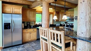 A kitchen with wooden cabinets, a stainless steel refrigerator, a wooden bar counter, and pendant lights.