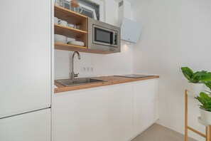 A modern kitchen with a built-in microwave, stainless steel sink, wooden shelves, and white cabinetry. - Sunny Guargacho6 Retreat—South Tenerife (Guargacho)