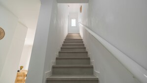 Eine Treppe mit weißen Wänden und einer Handläufung, die zu einem Raum mit einem Fenster führt.