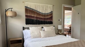 Een slaapkamer met een bed, nachtkastjes, een hangende macramé wandversiering en uitzicht op buiten.