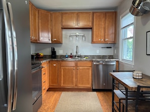 A kitchen with wooden cabinets, a stainless steel refrigerator, a dishwasher, and a granite countertop.