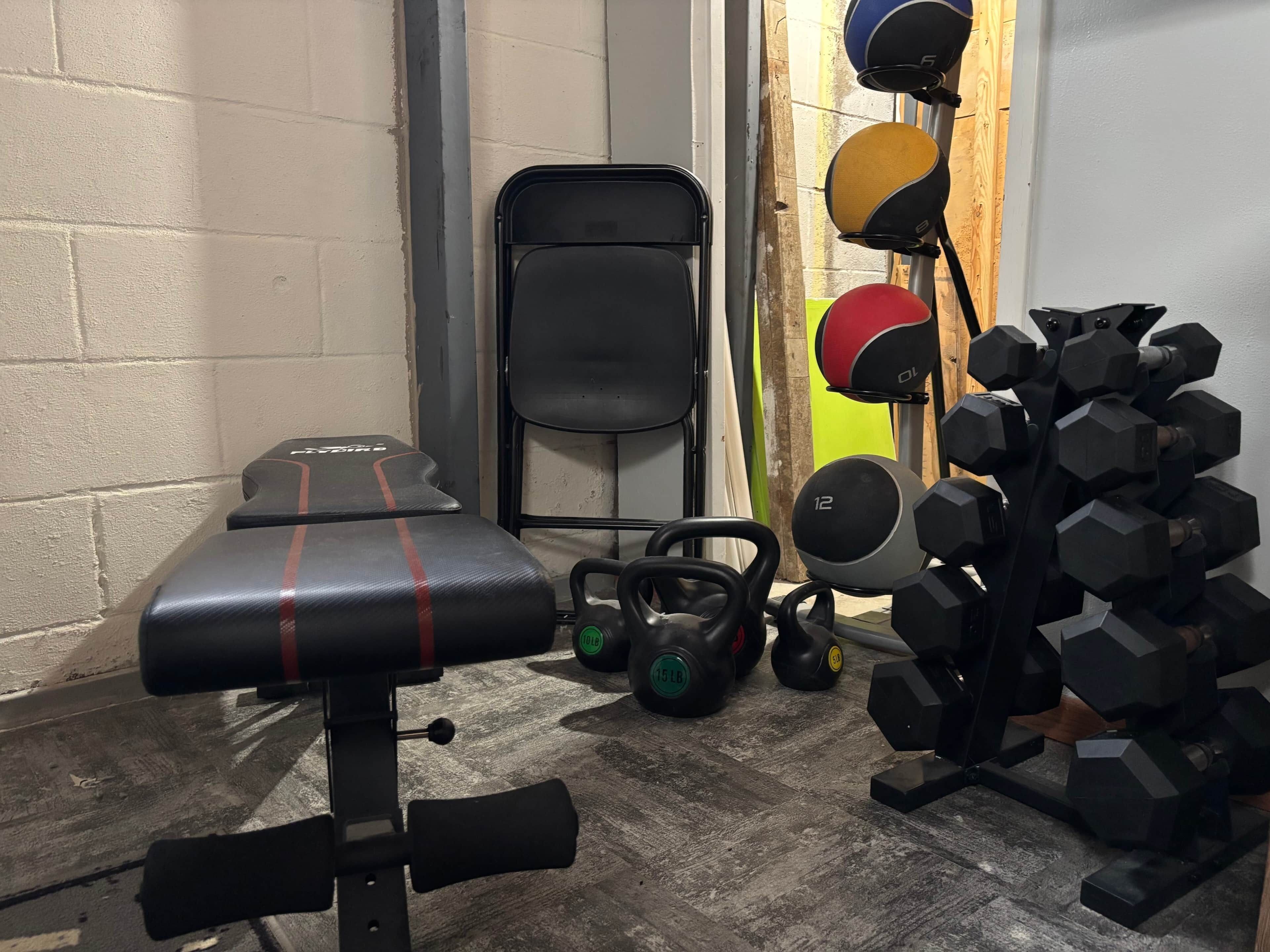 A gym with a bench, kettlebells, a squat rack, and a dumbbell rack.