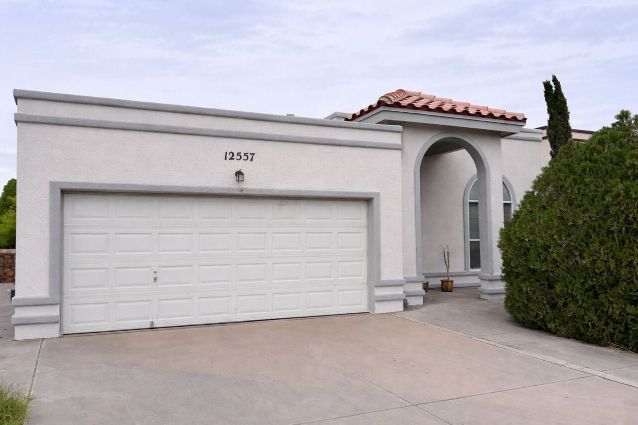 Une maison moderne avec un garage blanc, un toit recouvert de tuiles rouges et une grande porte d’entrée en arc de cercle.