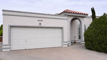 Une maison moderne avec un garage blanc, un toit recouvert de tuiles rouges et une grande porte d’entrée en arc de cercle.