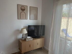 A living room with a TV on a wooden cabinet, a lamp, and two abstract wall art pieces. - One-bedroom apartment in Carnon, a 1-minute walk from the beach (Mauguio)