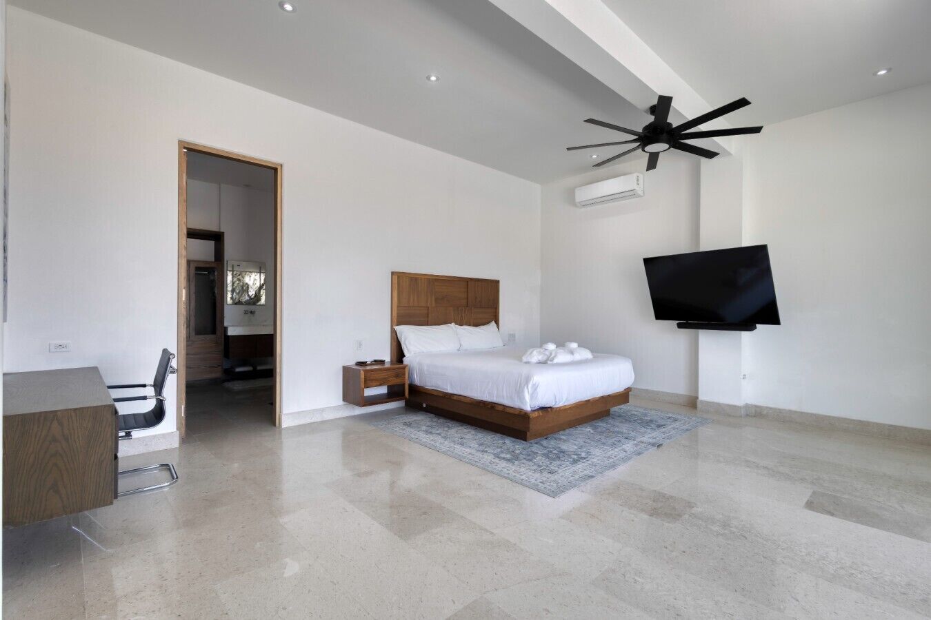 Een moderne slaapkamer met een bed, nachtkastjes, een bureau, een televisie en een airconditioning.