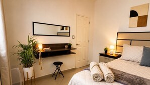 Ein Schlafzimmer mit Bett, Nachttisch, Lampe, Topfpflanze und Spiegel an der Wand.