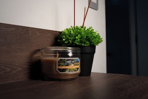 Eine Kerze in einem Glas mit dem Aufdruck 'Island Coconut Mahogany' neben einem Topfpflanzen auf einer Holztischfläche.