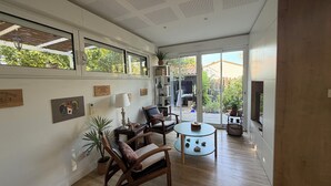Een ruime woonkamer met een groot raam, een houten vloer, een ronde salontafel en een boekenkast.